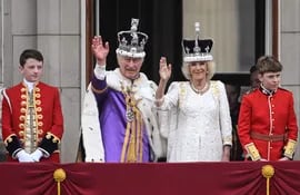 El rey Carlos III de Gran Bretaña con la corona del estado imperial y la reina Camila de Gran Bretaña con una versión modificada de la corona de la reina María saludan desde el balcón del Palacio de Buckingham después de ver el vuelo de la Royal Air Force en el centro de Londres el 6 de mayo de 2023, después de sus coronaciones.