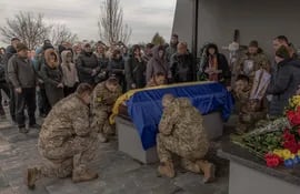 Soldados ucranianos se hincan de rodillas junto al ataúd de un camarada asesinado.