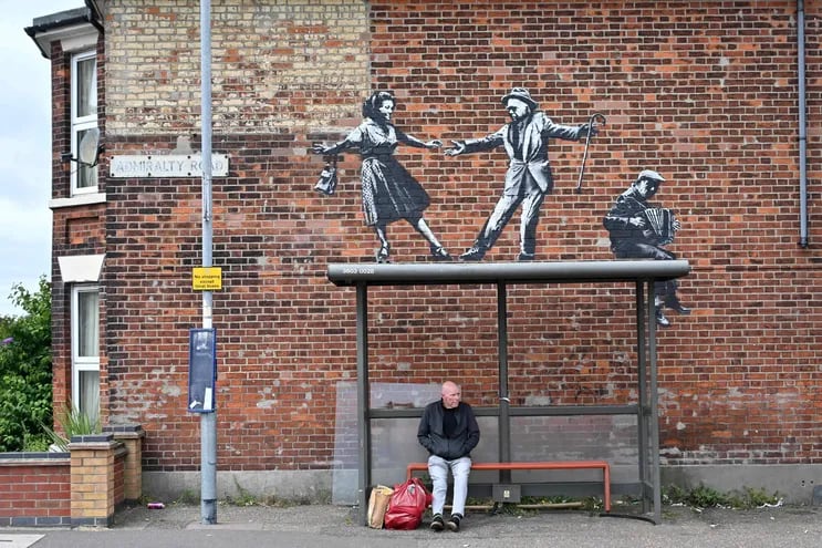 Un hombre espera el bus debajo de una pieza de arte que representa a una pareja bailando al son de un acordeón en Great Yarmouth, Inglaterra.