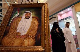 Un hombre y una mujer caminan junto a un retrato del presidente emiratí Khalifa bin Zayed al Nahyan, fallecido hoy.