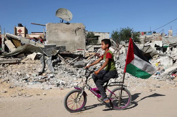 Un niño palestino en bicicleta junto a los escombros de un edificio destruido por recientes bombardeos israelíes en la ciudad de Rafah.
