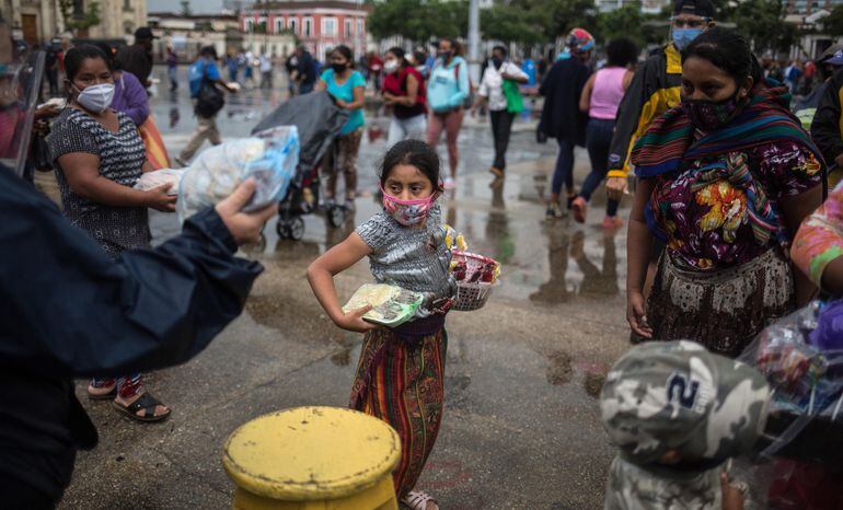 Una niña que vende dulces en la calle recibe uno de los almuerzos gratuitos en el Parque de la Constitución de Guatemala. El proyecto  privado “La olla comunitaria” culminará su labor tras servir 100.000 almuerzos durante la pandemia y desnudar aún más la realidad del país, en el que uno de cada dos niños sufre de desnutrición y  hambre, acentuadas por la pandemia.