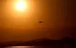Un sol abrasador tiñe de naranja el cielo mientras helicópteros cargan agua para combatir un incendio forestal. (EFE)