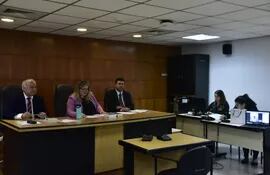 El Tribunal de Sentencia, presidido por la jueza Elsa García e integrado por sus colegas Víctor Medina y Darío Báez, en la audiencia de revisión de medidas a Enzo Cardozo (en pantalla de la notebook).