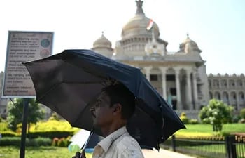 Un hombre se refugia bajo un paraguas en un caluroso día de verano cerca de Vidhana Soudha, la Asamblea Legislativa del Estado, en Bengaluru.