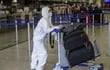 Un pasajero con traje protector empuja un carrito de equipaje en el Aeropuerto Internacional de Frankfurt.