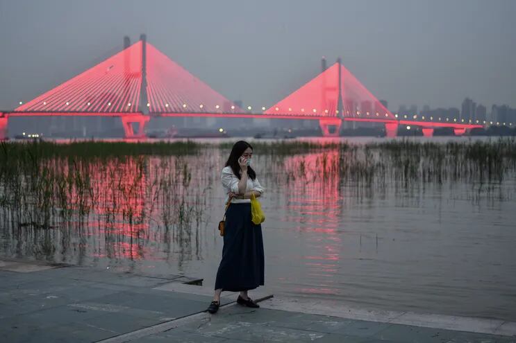 Una mujer con mascarilla como medida preventiva contra el coronavirus Covid-19 habla por teléfono junto al río Yangtze en Wuhan donde se originó la pandemia.