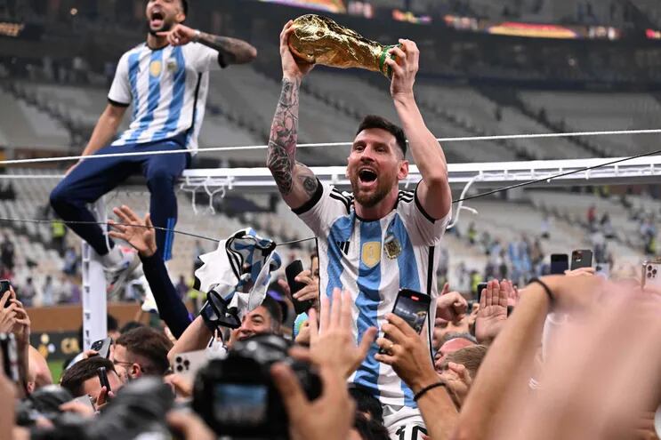 El delantero número 10 de Argentina, Lionel Messi, levanta el trofeo de la Copa Mundial de la FIFA mientras celebra con sus seguidores ganar la final de la Copa Mundial de Qatar 2022 entre Argentina y Francia en el Estadio Lusail de Lusail, al norte de Doha, el 18 de diciembre de 2022.