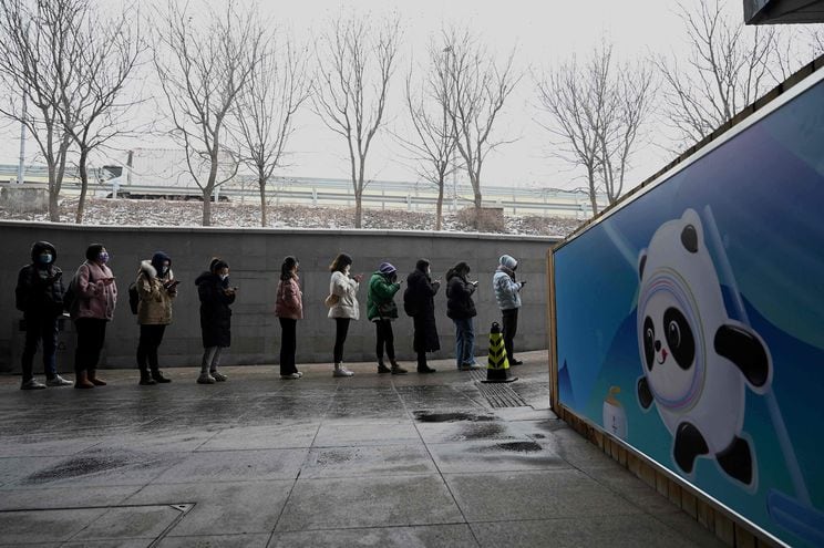Gente formando fila para hacerse el test de Covid, junto a un poster que muestra a Bing Dwen Dwen, mascota de los juegos olímpicos 2022.