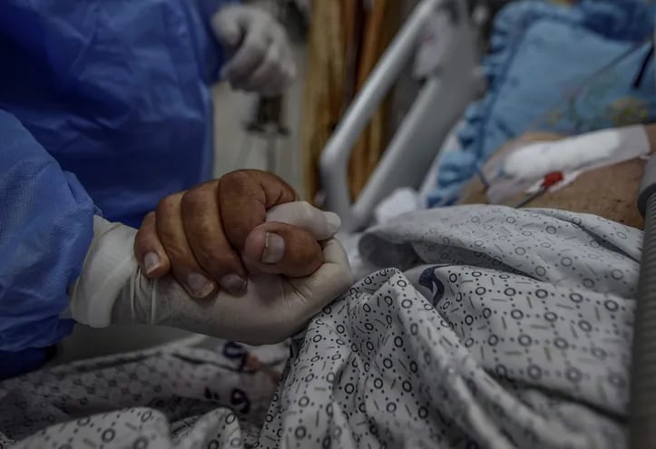 Un sanitario agarra la mano de un paciente en una unidad de cuidados intensivos.