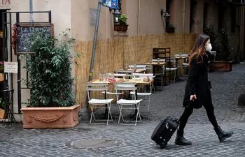A woman wearing protective mask pulls a trolley bag as she walks past empty cafe tables as the government brings in new restriction measures to curb the spread of COVID-19 novel coronavirus,  in central Rome on November 5, 2020. (Photo by ANDREAS SOLARO / AFP)