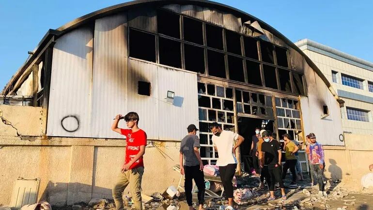 Varios curiosos inspeccionan el lugar tras el incendio declarado en un hospital de la ciudad de Nasiriya, en el sur de Irak, para tratar a los pacientes aislados con covid-19, ay que causó al menos 64 muertos y 50 heridos, según informaron fuentes oficiales.
