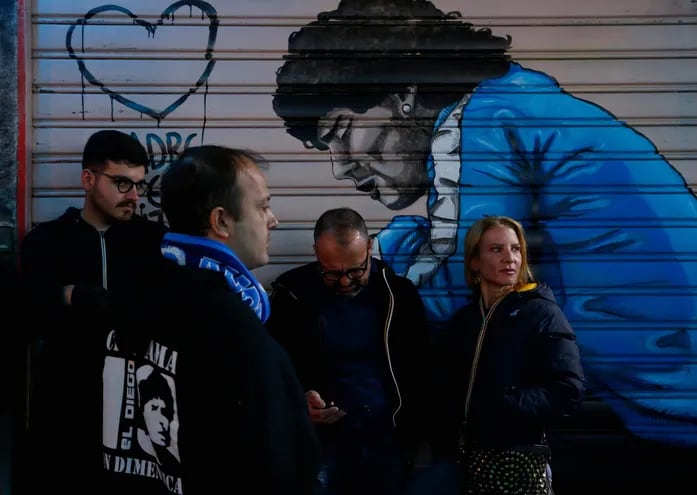 Seguidores del Napoli siguiendo por celulares el desenlace del partido de Lazio vs. Sassuolo, frente a un local con la pintura de Diego Maradona, ídolo máximo de los napolitanos.