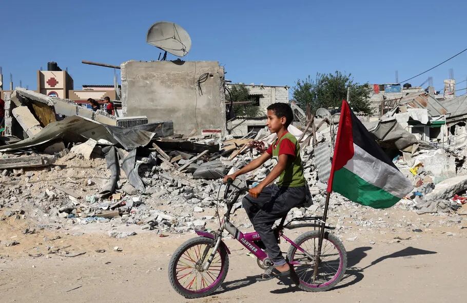 Un niño palestino pasa en bicicleta frente a las ruinas de un edificio recientemente destruido por un bombardeo israelí, en Rafah, al sur de Gaza.