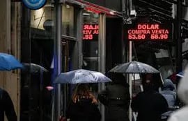Transeúntes caminan bajo la lluvia frente a carteles que informan el precio del peso argentino sobre la moneda extranjera en Buenos Aires, Argentina. (Imagen de archivo EFE ).