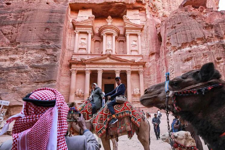 A tourist poses for a photo while riding a camel before the site of the Treasury at the ruins of the ancient Nabatean city of Petra in southern Jordan on December 12, 2022. - After years in which the Covid pandemic turned the storied "Rose City" into a ghost town, Jordan tourism authorities confirm that Petra, famous for its stunning temples hewn out of the rose-pink cliff faces, is back in business and drew 900,000 visitors last year, close to the previous record of one million set in 2019. (Photo by Khalil MAZRAAWI / AFP)
