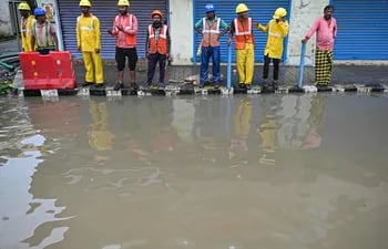 Hombres de pie junto a una acera a lo largo de una calle inundada después de las lluvias, mientras se espera que el ciclón Michaung toque tierra.