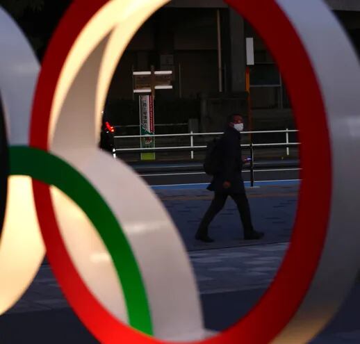 Un hombre con tapabocas camina en las inmediaciones de los anillos olímpicos instalados en Tokio.