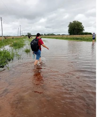 Una docente cruza a pie en la zona de Tacuara´i del distrito de Tacuaras para llegar a la ruta PY04 luego de que el vehículo que lo transportaba quedara atascado en el camino en medio del agua.