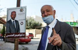 Un votante, enmascarado debido a la pandemia del coronavirus COVID-19, muestra su dedo manchado de tinta después de votar en Irbid, en el norte de Jordania.