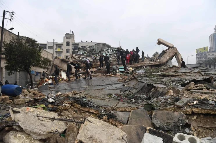 La gente se reúne alrededor de los edificios derrumbados mientras los equipos de rescate buscan sobrevivientes después de un terremoto en la ciudad siria de Alepo, controlada por el gobierno.