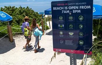 Fotografía y referencia: una pareja mientras camina frente a una placa con indicaciones y restricciones en la playa de Miami Beach, Florida (EE.UU).