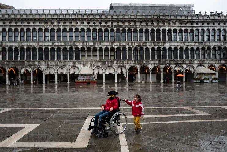 Dos niños juegan con una silla de ruedas en una desierta plaza de San Marcos, en Venecia, Italia. Su tradicional carnaval fue cancelado, debido a la pandemia de covid-19.