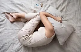 Una mujer con depresión se acurruca en una cama y se tapa la cara con una almohada.
