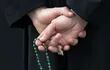 Un sacerdote sostiene un rosario entre sus dedos.