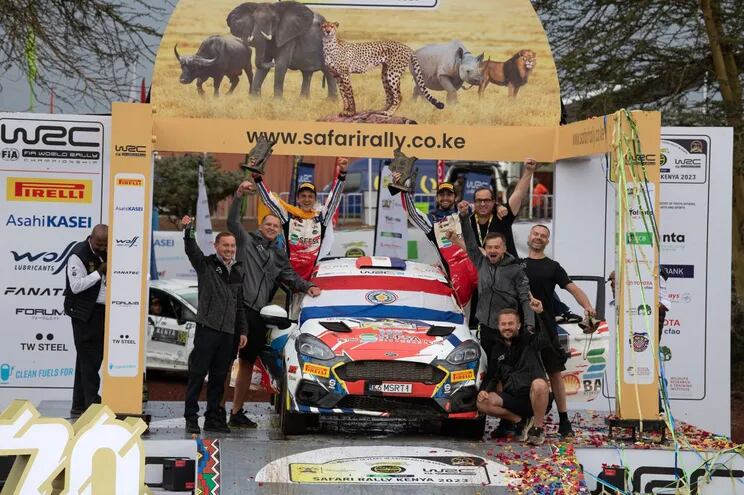 El piloto Diego Domínguez Bejarano, con la bandera paraguaya extendida  sobre el Ford Fiesta Rally3 Evo, festeja su tercer triunfo en el WRC junto a su padre Diego y el español Rogelio Peñate