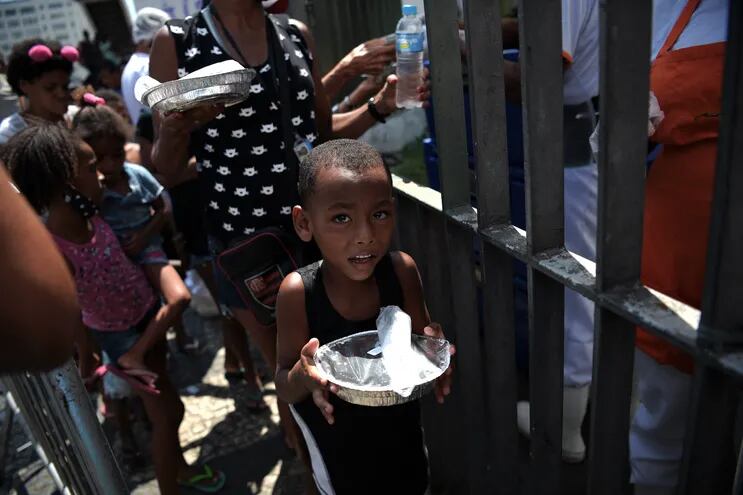 Un niño recibe un plato de comida luego de formar fila frente a un centro de distribución de alimentos en Río de Janeiro, Brasil.