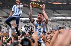 El delantero número 10 de Argentina, Lionel Messi, levanta el trofeo de la Copa Mundial de la FIFA mientras celebra con sus seguidores ganar la final de la Copa Mundial de Qatar 2022 entre Argentina y Francia en el Estadio Lusail de Lusail, al norte de Doha, el 18 de diciembre de 2022.