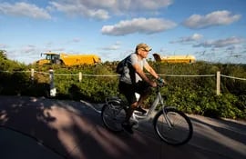 Un hombre pasea en bicicleta cerca de la maquinaria pesada usada para rellenar la costa de Miami Beach.