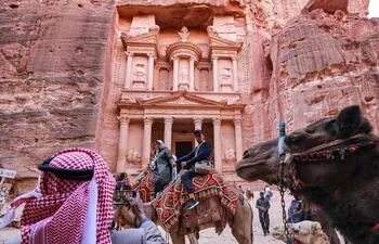 A tourist poses for a photo while riding a camel before the site of the Treasury at the ruins of the ancient Nabatean city of Petra in southern Jordan on December 12, 2022. - After years in which the Covid pandemic turned the storied "Rose City" into a ghost town, Jordan tourism authorities confirm that Petra, famous for its stunning temples hewn out of the rose-pink cliff faces, is back in business and drew 900,000 visitors last year, close to the previous record of one million set in 2019. (Photo by Khalil MAZRAAWI / AFP)