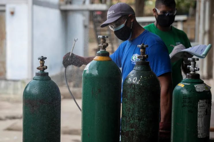 Dos trabajadores desinfectan cilindros de oxígeno.