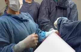 tres personas den batas celestes, tapabocas blancas durante una operación