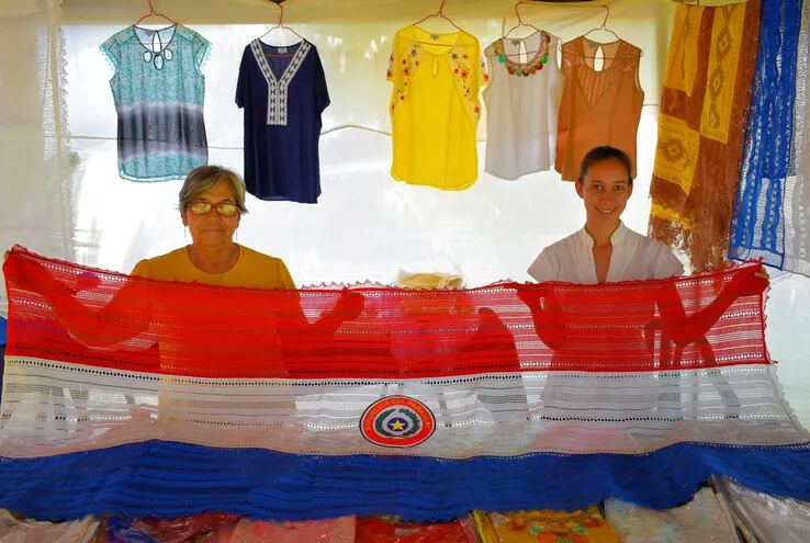 Las artesanas Antonia de Cabral y Liz Cristaldo exhibiendo una hermosa bandera paraguaya de ao po'i de 2 metros, que tiene un costo de apenas G. 400 mil.