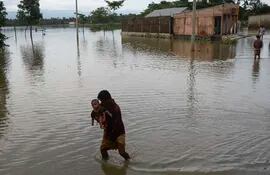 Un hombre con un niño en brazos cruza un área inundad en Sunamgong, Bangladés.
