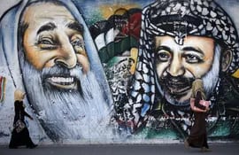 Mujeres caminan frente a un mural con ilustraciones de líderes palestinos.