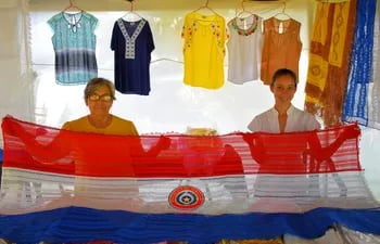 Las artesanas Antonia de Cabral y Liz Cristaldo exhibiendo una hermosa bandera paraguaya de ao po'i de 2 metros, que tiene un costo de apenas G. 400 mil.