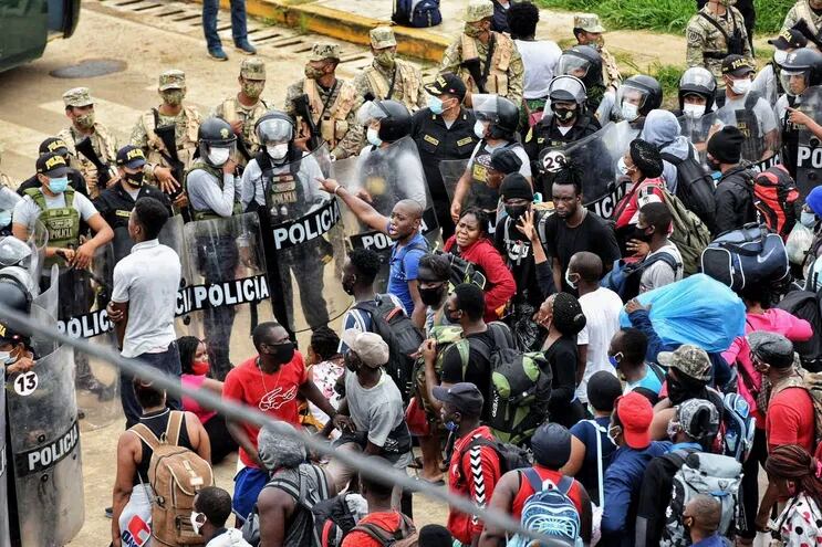 Migrantes haitianos, presentes en el Brasil, intentan cruzar un bloqueo policial de la policía peruana en la frontera entre ambos países.