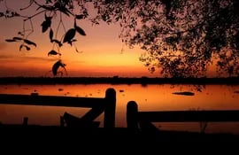 Sinfonía en naranja a orillas del río Paraguay. El amanecer tiene como telón sonoro el canto de las aves, la música paraguaya y el correr del agua.