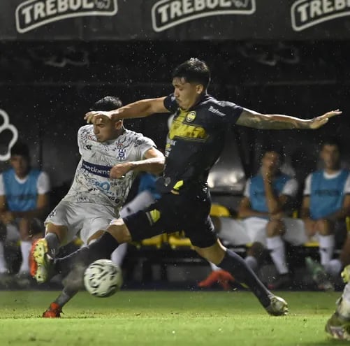 El volante del 2 de Mayo Víctor Argüello  saca un potente remate ante la apresurada llegada del defensor de Sportivo Trinidense Juan Vera.