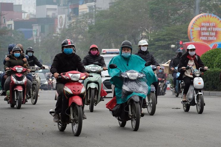 Personas protegidas con mascarillas viajan en motocicletas por una calle de Hanoi, Vietnam.