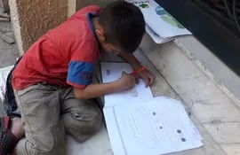 Un niño estudia con folletos en una vereda del centro asunceno.