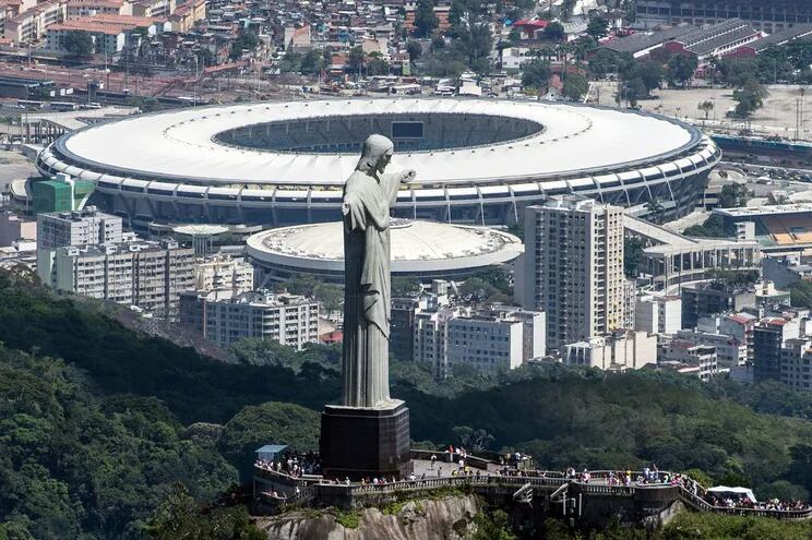 El Cristo Redentor o Cristo del Corcovado con los brazos abiertos mostrando a la ciudad de Río de Janeiro. Al fondo, el estadio Maracaná, que será sede de la final.
