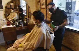 Tote Pascual, con un protector facial y mascarilla, le corta el pelo a un cliente, que también usa mascarilla.