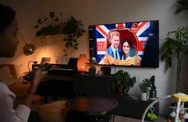 Una mujer mira en el televisor de su sala los primeros episodios de la serie "Harry y Meghan" sobre los duques de Sussex.