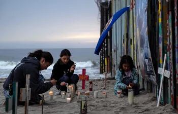 Tres personas encienden velas durante un evento en conmemoración de los fallecidos en su intento de cruzar a Estados Unidos en Playas de Tijuana, Baja California (México).