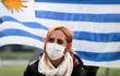 Una mujer protegida con tapabocas se ve frente a una bandera de Uruguay este miércoles, en Montevideo (Uruguay). El presidente de Uruguay, Luis Lacalle Pou, anunció este miércoles que su país tiene capacidad sanitaria para 8.700 casos, 622 de ellos graves, de la enfermedad de la COVID-19.